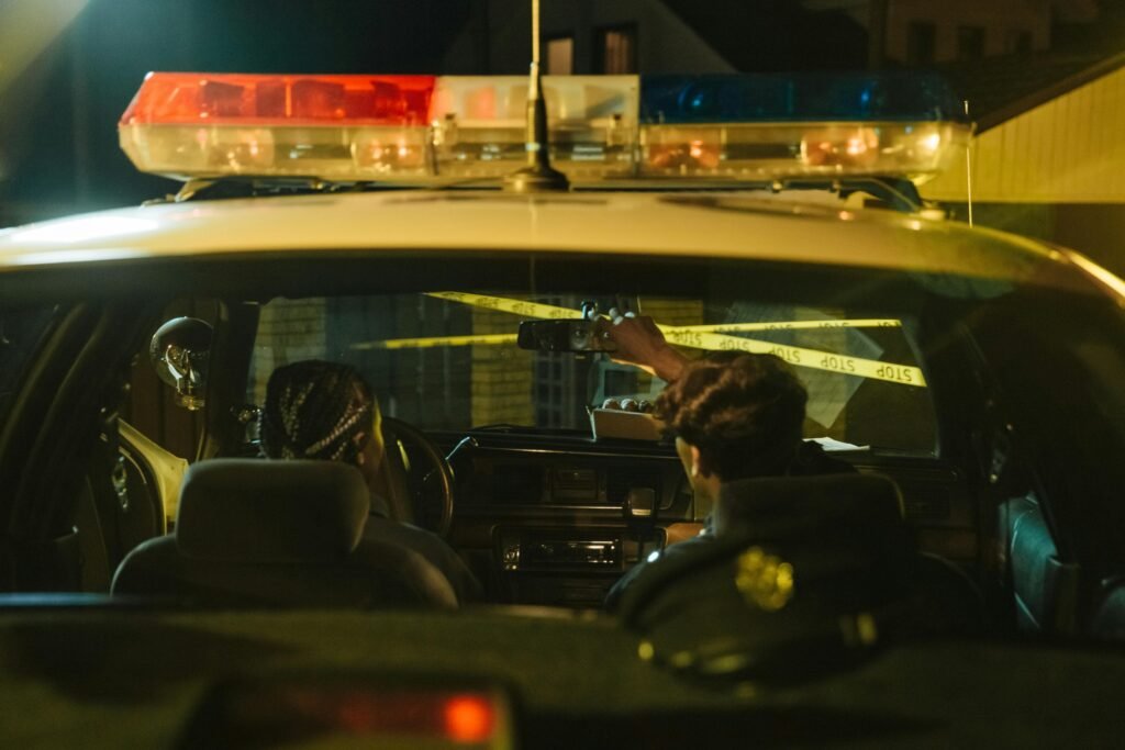 Police officers monitoring a scene through rearview mirror at night with caution tape visible.