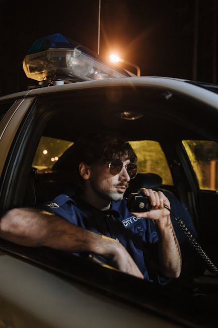 Nighttime shot of a police officer in sunglasses using a radio in a patrol car.